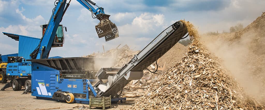 Broyeur FORUS SE 25 et pelle FUCHS transformant des déchets de bois en copeaux sur un site industriel.
